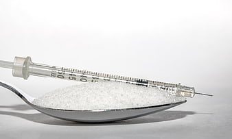 Insulin syringe on spoon with white sugar