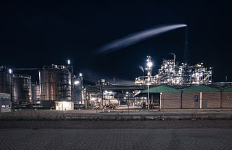 Illuminated industrial factory complex at night with smokestack