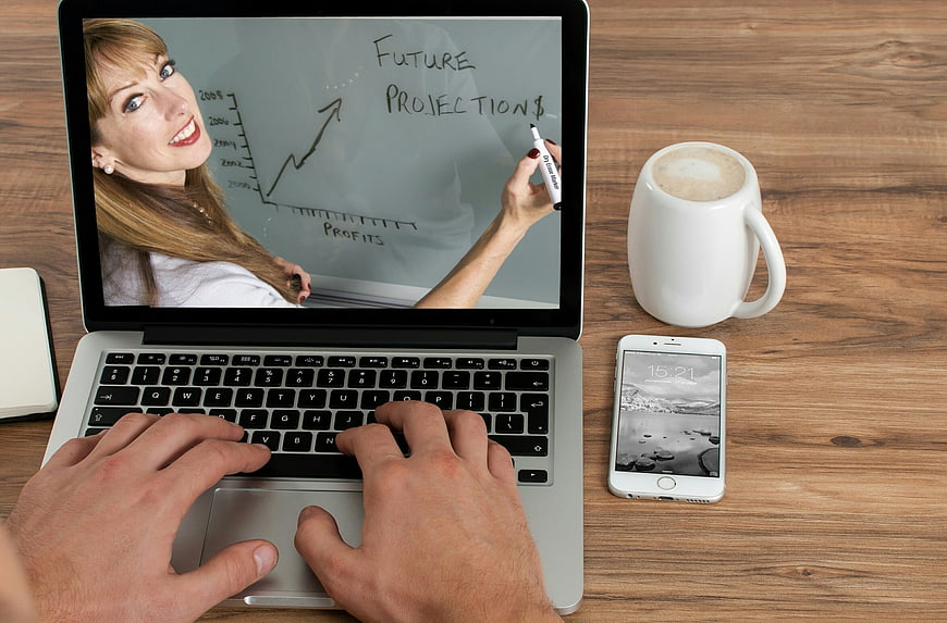Businessman typing on laptop with online training video of female teacher