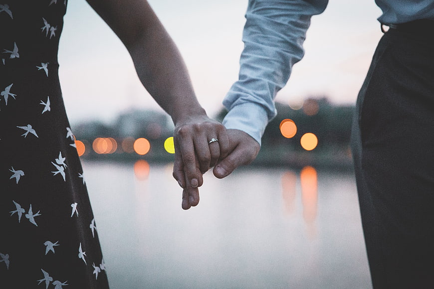 Couple Holding Hands with Engagement Ring by Water at Dusk