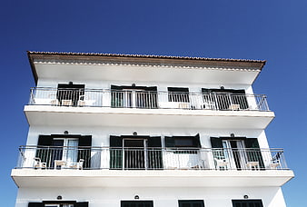 White Mediterranean Apartment Building with Balconies Against Blue Sky