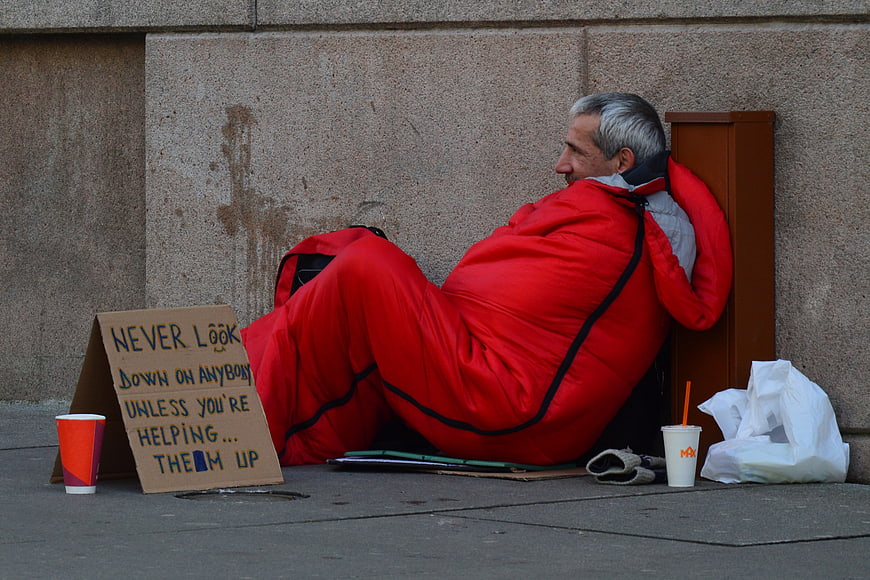 Homeless man in red sleeping bag with cardboard sign