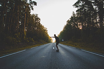 Skateboarder Riding Down Forest Road at Sunset