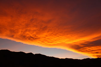 Dramatic fiery orange sunset sky over dark mountain silhouette