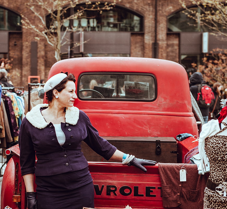Vintage woman in retro outfit standing by red classic truck