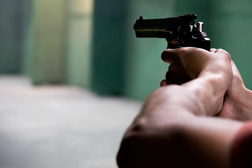 Close-up of hands aiming a black pistol at a shooting range