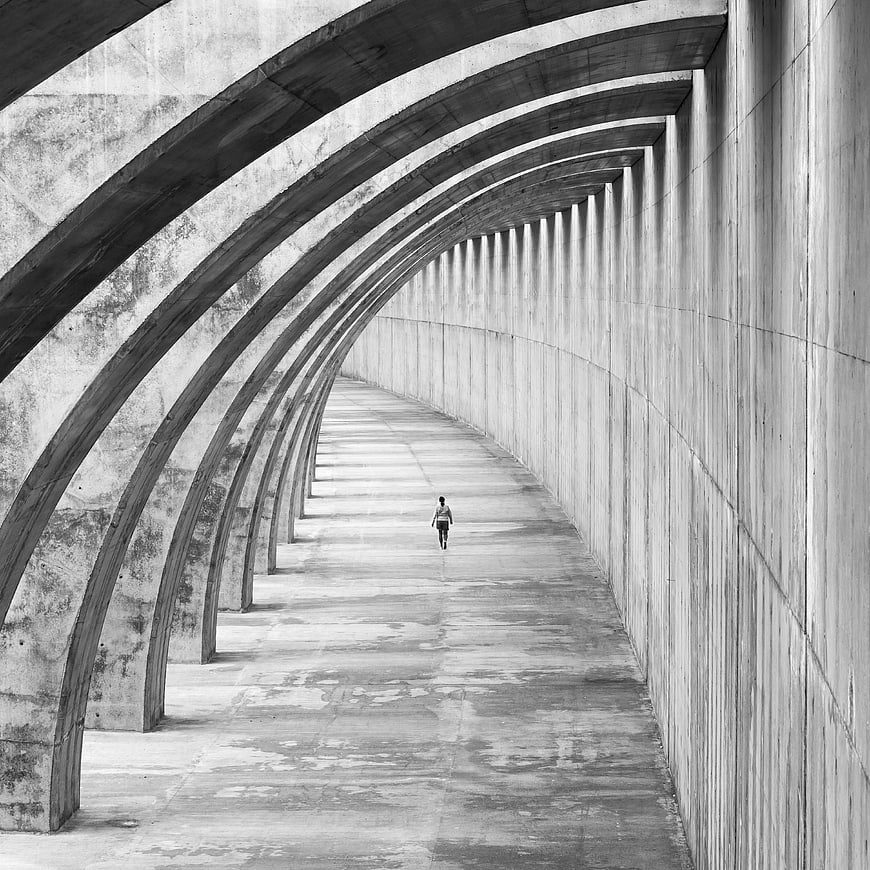 Monochrome Concrete Arch Corridor With Lone Walking Figure