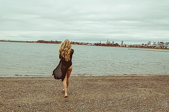 Blonde Woman in Black Dress Walking on Pebble Beach