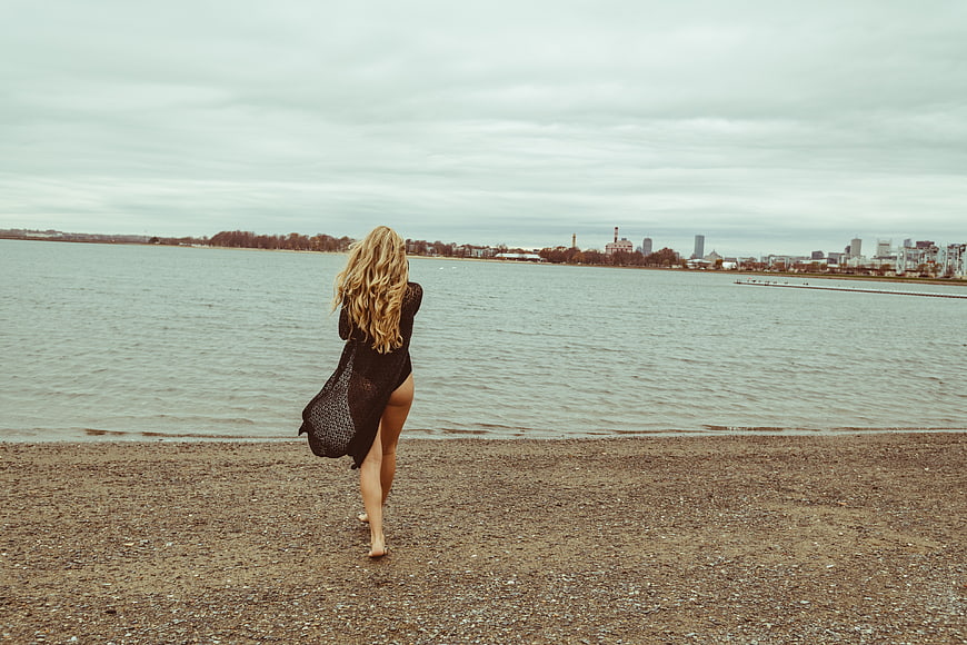 Blonde Woman in Black Dress Walking on Pebble Beach