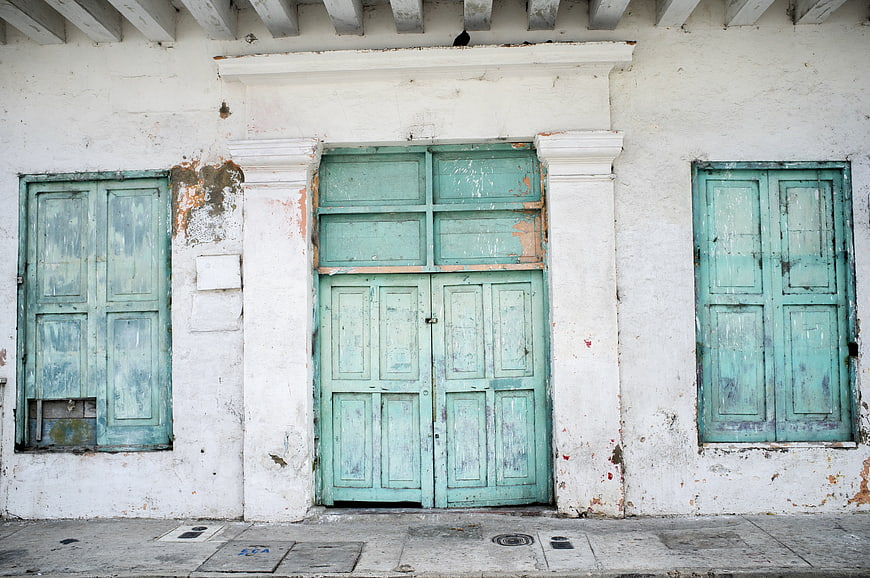 Weathered Turquoise Wooden Doors On White Colonial Facade
