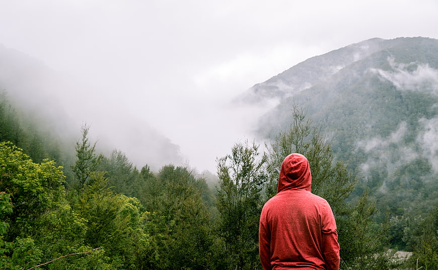 Man in Red Hoodie Looking at Misty Mountain Landscape