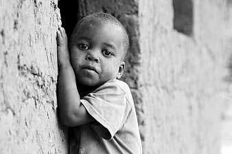Black and white portrait of young African child leaning against wall