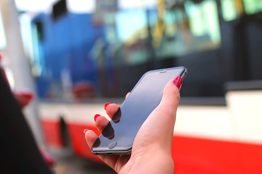 Woman holding smartphone with red nails near bus