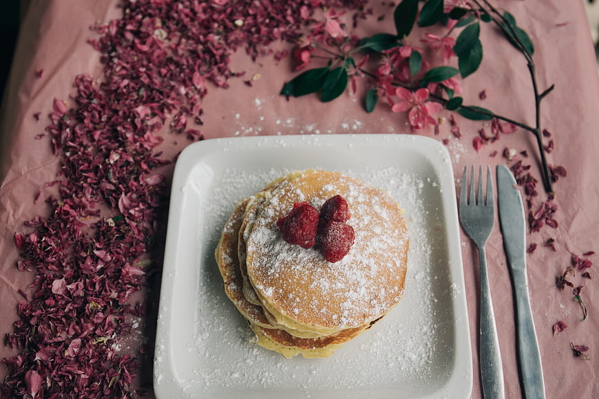 Stack of pancakes with raspberries and powdered sugar on pink table