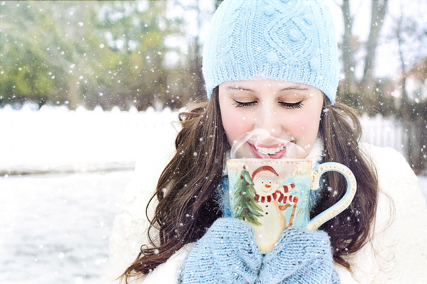 Woman sipping hot drink from Christmas mug in snow