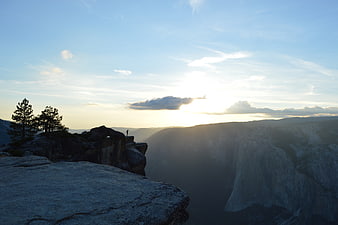 Silhouette of Hiker on Rocky Cliff Overlooking Mountain Valley at Sunset