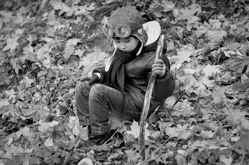 Child in Aviator Hat Sitting in Autumn Leaves