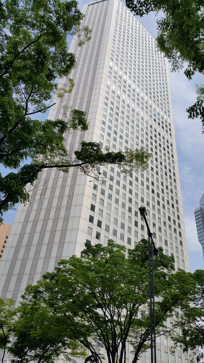 Low angle view of modern white skyscraper with green trees