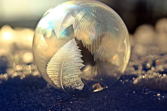 Frozen soap bubble with intricate ice crystals on blue surface