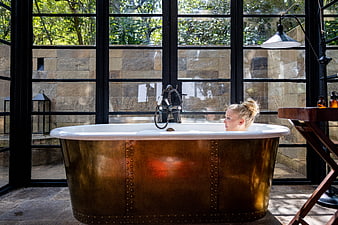 Woman relaxing in copper bathtub by large windows