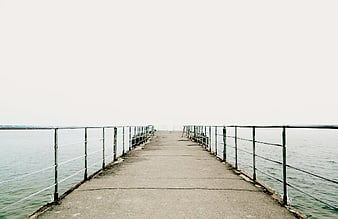 Minimalist concrete pier extending into calm sea with metal railings