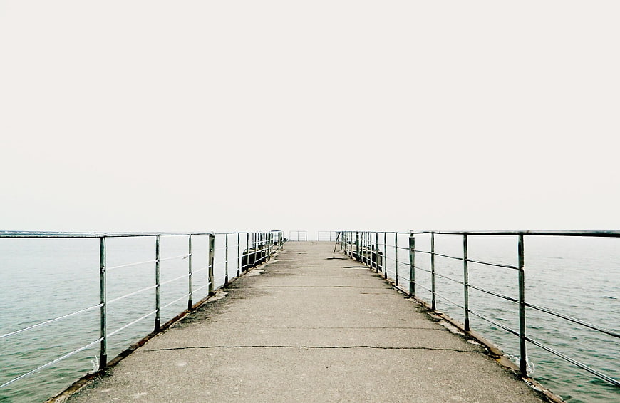 Minimalist concrete pier extending into calm sea with metal railings