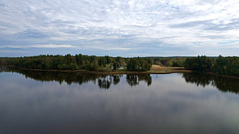 Aerial view of calm lake with forest shoreline and cloudy sky