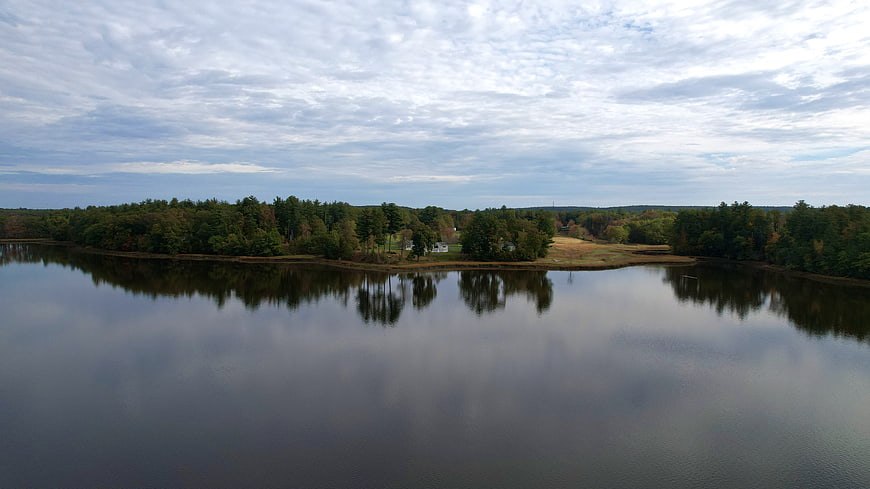 Aerial view of calm lake with forest shoreline and cloudy sky