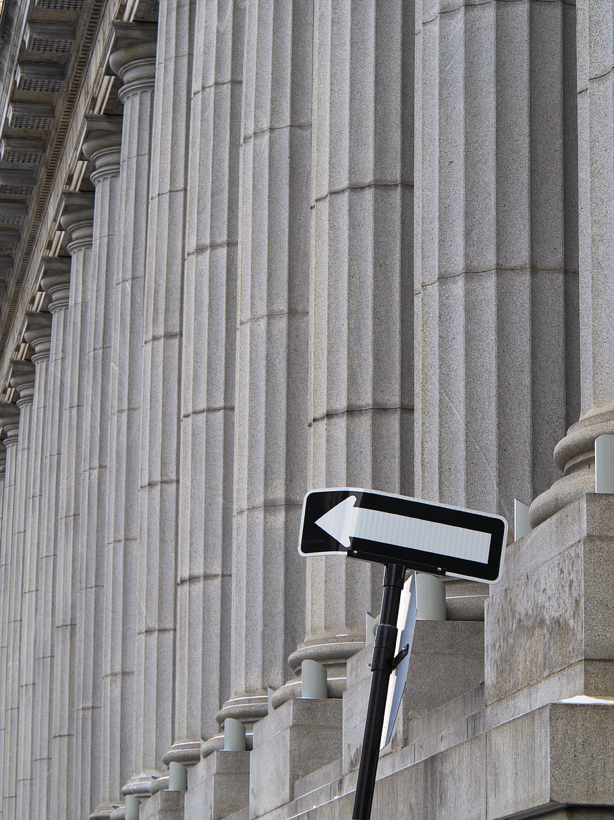 Directional arrow sign in front of classical stone columns