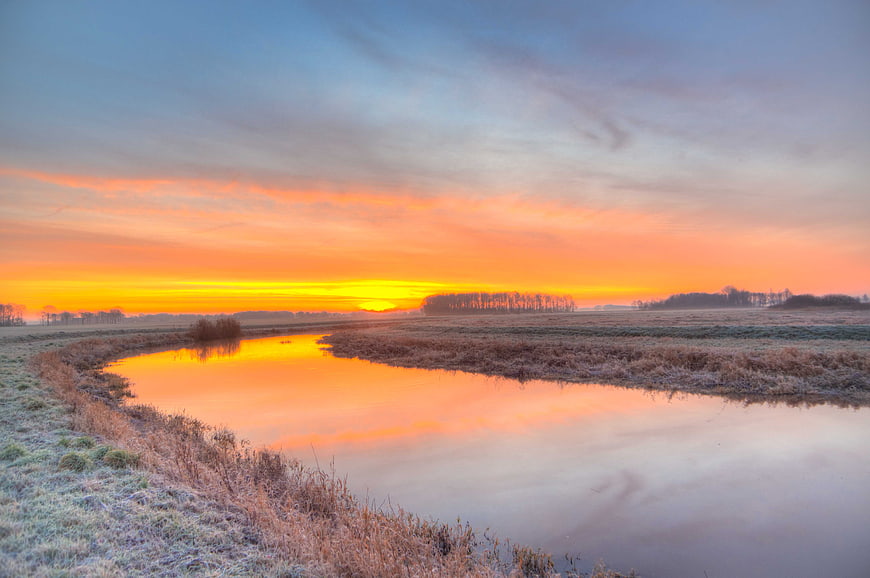 Vibrant sunrise over a calm river with frosty banks