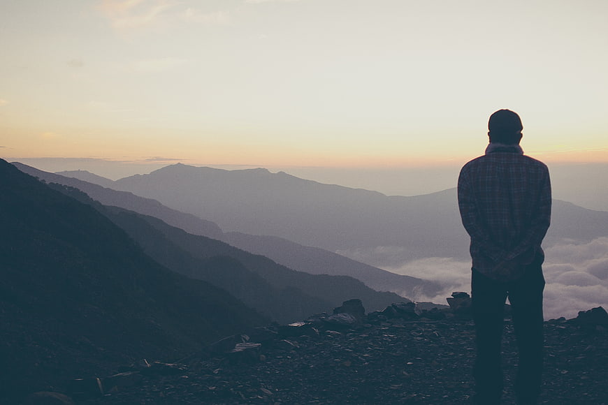Man Standing On Mountain Ridge Watching Sunset Over Clouds