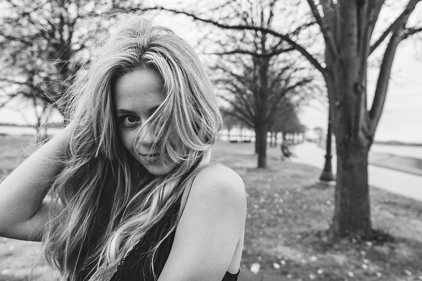 Black and white portrait of young woman with windblown hair in park