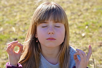 Young girl meditating outdoors with eyes closed in a peaceful field