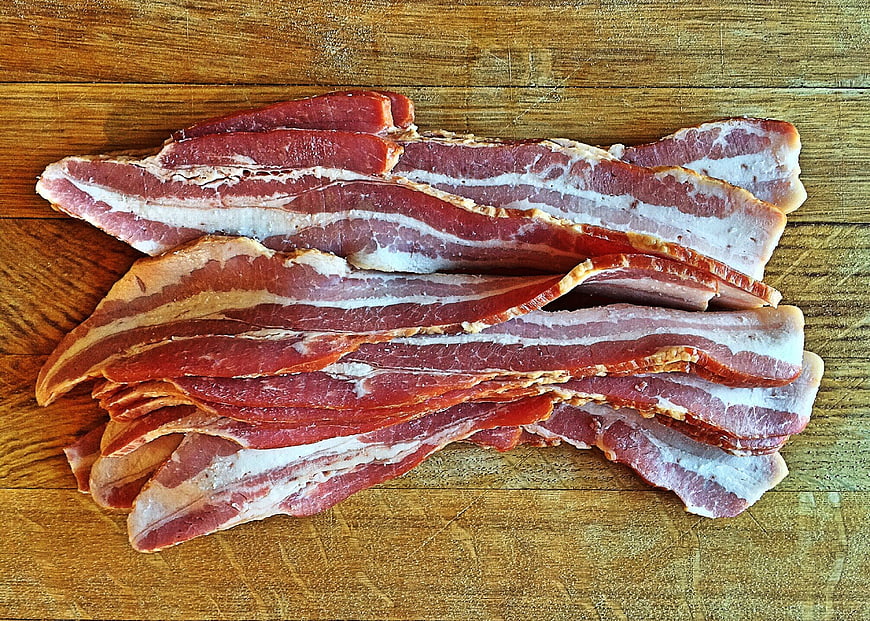 Raw bacon strips on wooden cutting board