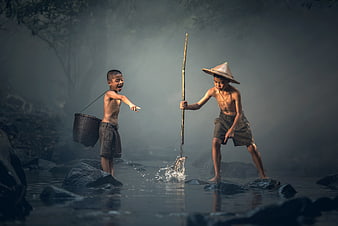 Two young boys fishing in a misty river with traditional gear