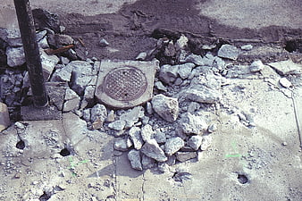 Broken concrete sidewalk with exposed manhole cover and rubble