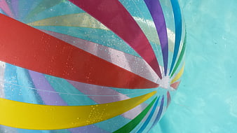 Colorful striped beach ball floating in blue pool water