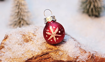 Red Christmas Ornament with Gold Snowflake on Snowy Wood