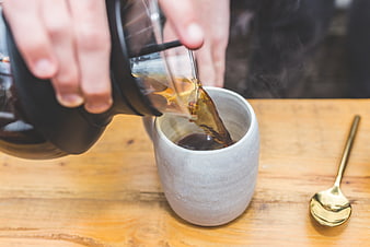 Pouring hot coffee from carafe into ceramic mug on wooden table