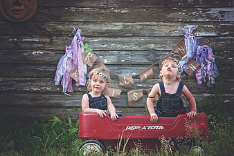 Two young girls in denim overalls posing in a red Radio Flyer wagon