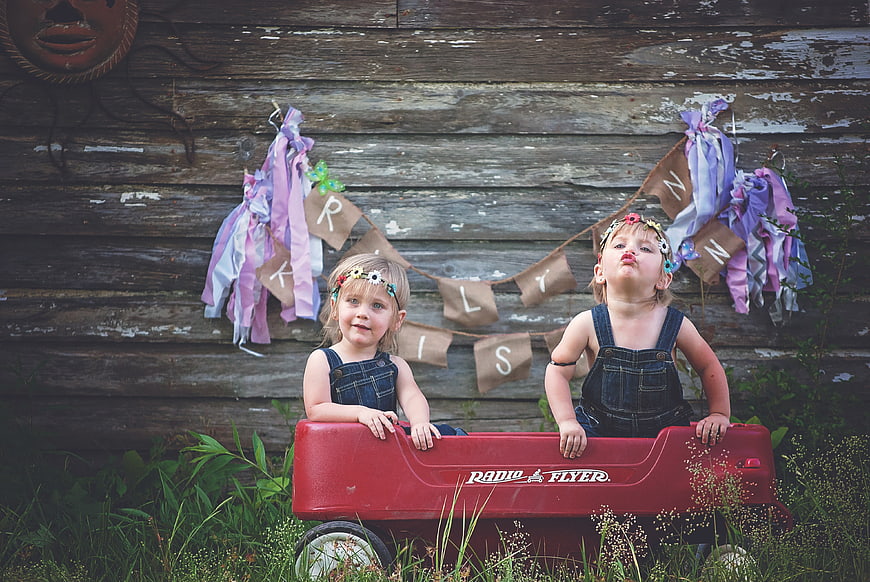 Two young girls in denim overalls posing in a red Radio Flyer wagon