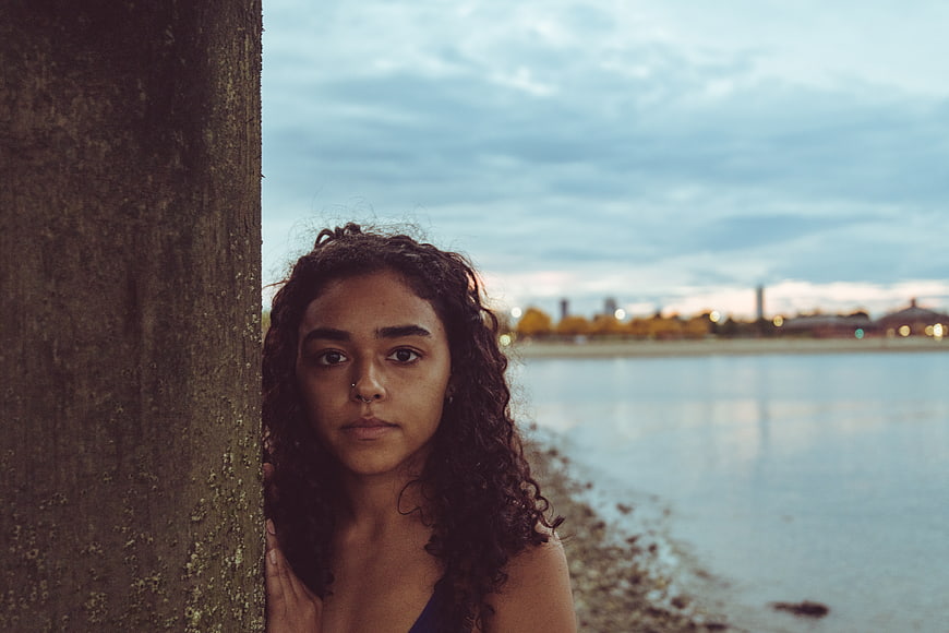 Serious Woman Portrait Leaning Against Tree by Lake