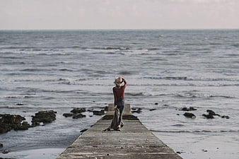 Woman Standing on Wooden Pier Looking at Ocean