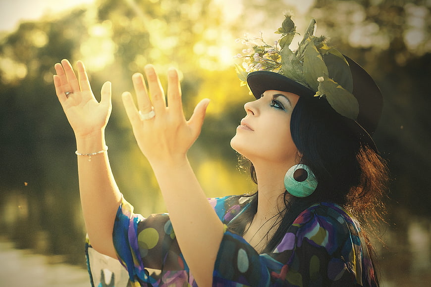 Woman with floral hat reaching for sunlight in nature