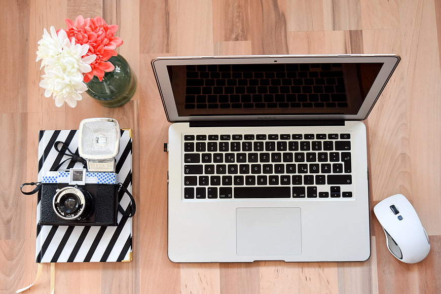 Flat lay workspace with laptop, camera, and flowers