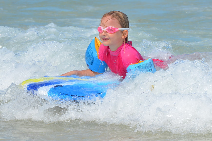 Young Girl Surfing on Blue Board in Ocean Waves