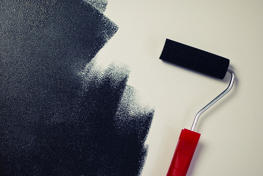 Black paint roller on white wall with fresh paint stroke