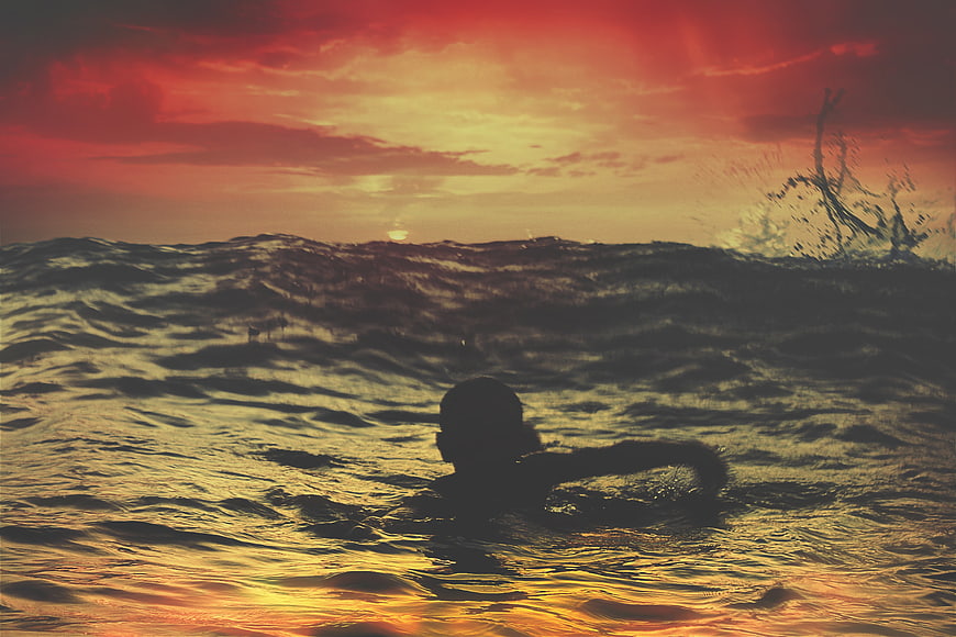 Silhouette of Child Swimming in Ocean at Sunset