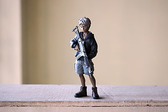 Anime Boy Figurine Holding Gun On Wooden Surface