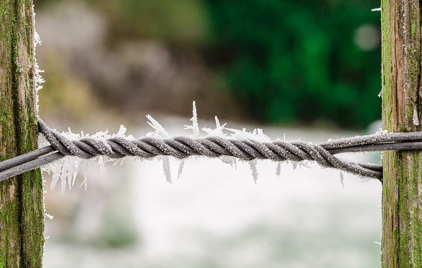 Frost-covered twisted wire between wooden fence posts